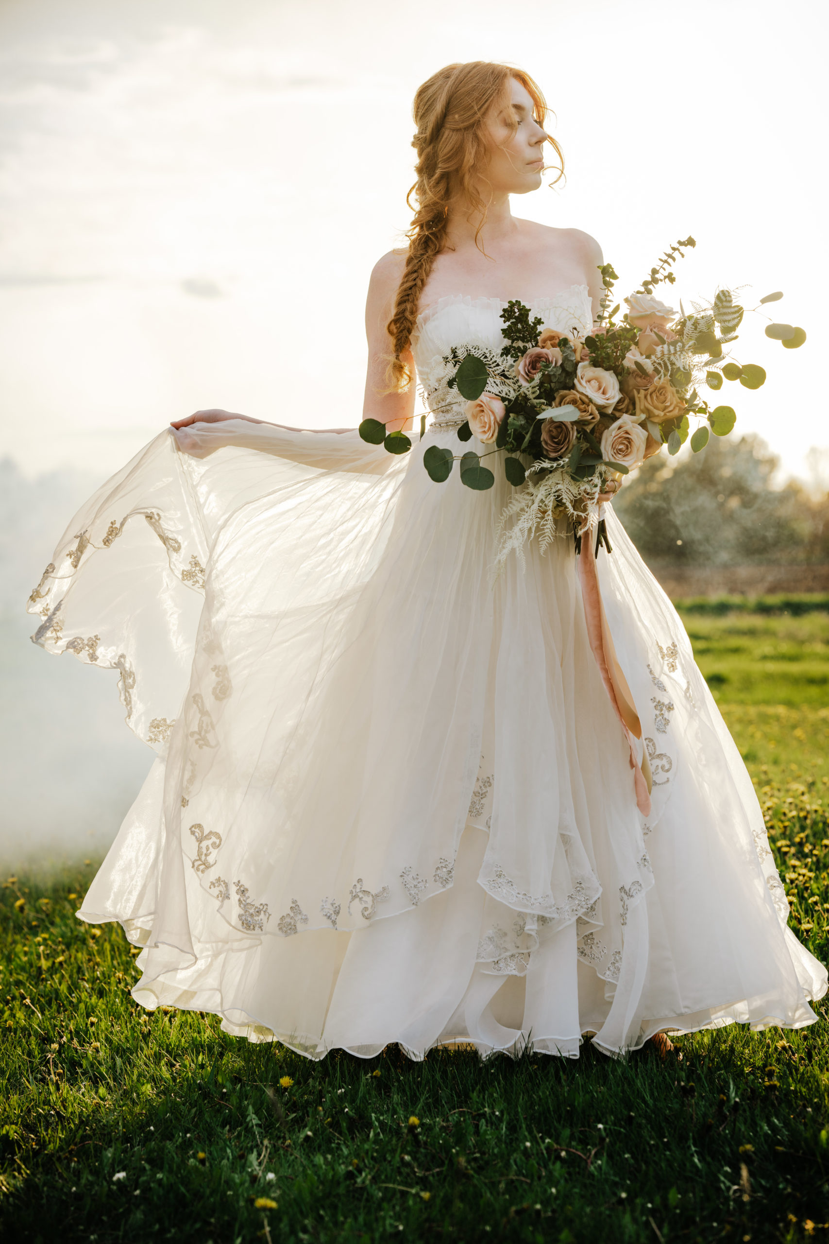 Bride in a field holding a bouquet at sunset