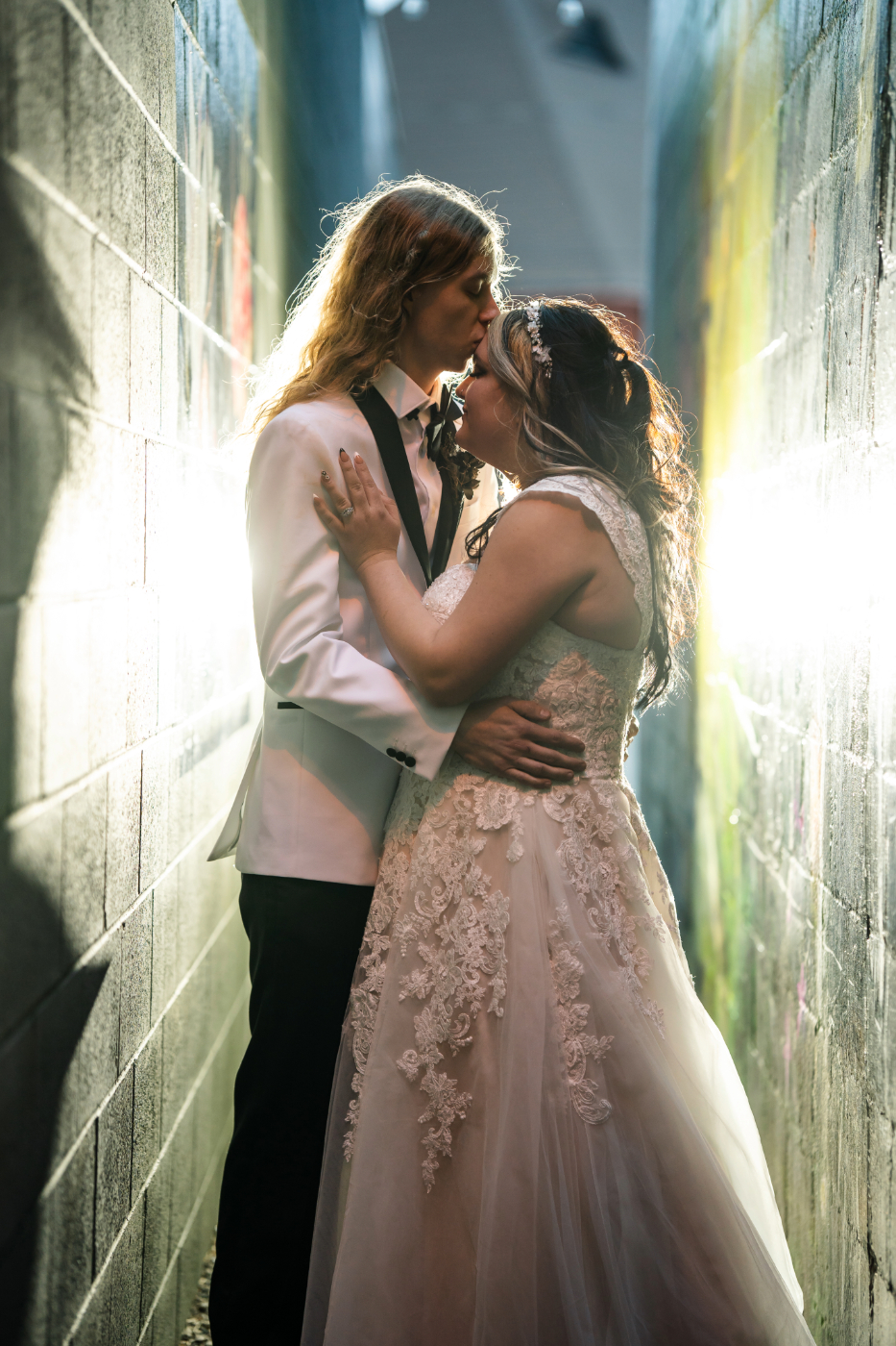 Bride and groom sharing an intimate moment in an alleyway, captured by an Oshkosh, Wisconsin wedding photographer with sunlight illuminating them from behind.