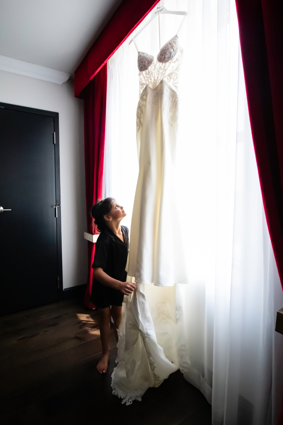 Bride's daughter looking up at her mother's wedding dress hanging in the window on the wedding day at Hotel Retlaw in Fond Du Lac, Wisconsin