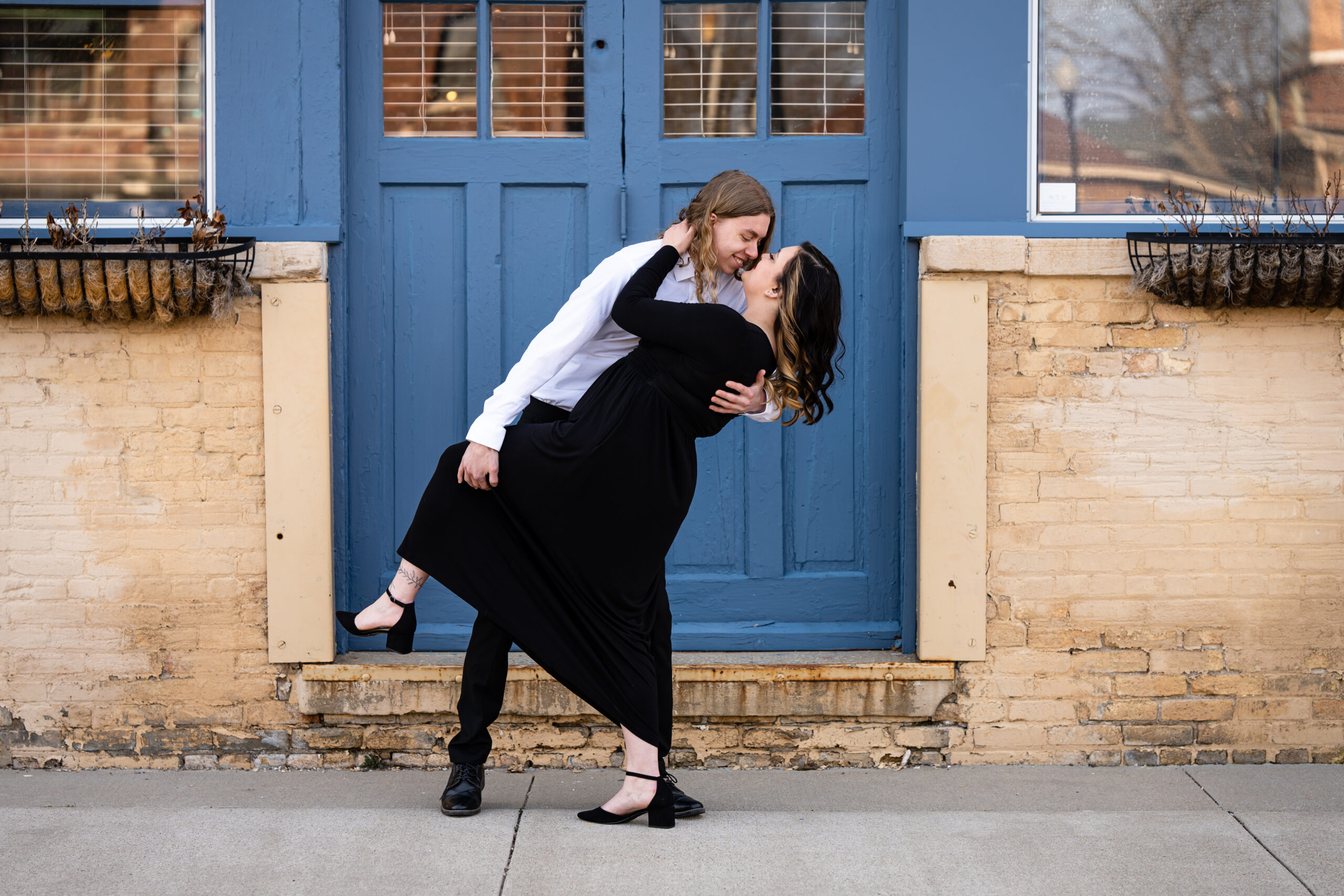 A couple sharing a romantic dip in front of a blue door during their engagement photo session, captured by a wedding photographer in Oshkosh, Wisconsin